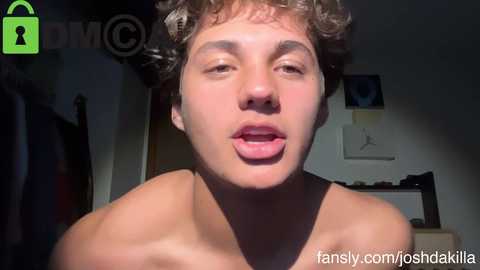 Video of a shirtless, curly-haired, light-skinned young man with a slightly open mouth, in a dimly lit bedroom with a green padlock watermark in the corner.