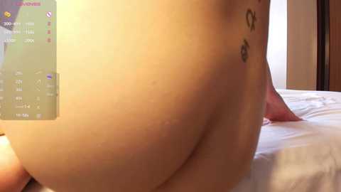 Video of a naked, light-skinned person with a tattoo on their backside, lying on a bed. A digital display showing health metrics is visible.