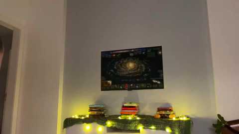A video of a cozy indoor scene featuring a wall-mounted TV displaying a game, a green garland with white lights, and a stack of colorful books on a wooden shelf.