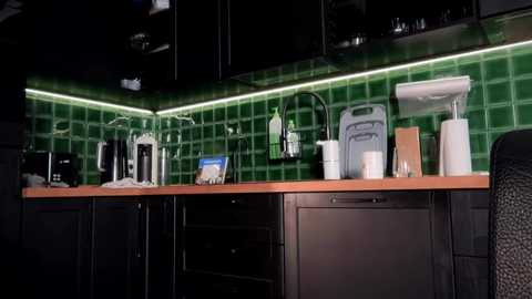 Media: A video of a modern kitchen with dark wood countertops, green-tiled backsplash, stainless steel appliances, and a laptop on the counter. The space has a sleek, minimalist design.