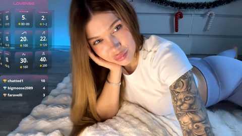 Video of a light-skinned woman with long brown hair, lying on a white furry rug, wearing a white crop top and grey leggings, showcasing a detailed tattoo sleeve.