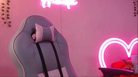 Video of a pastel blue gaming chair with a white pillow, in a room with pink neon heart-shaped lights and green vines on the wall.