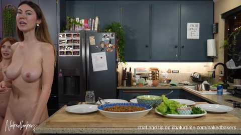 Video of a modern kitchen with a nude woman standing by the counter, cooking with a man and a child. Dark cabinets, stainless steel appliances, and a wooden countertop.