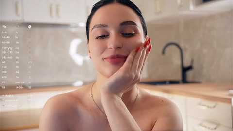 Media: Video of a light-skinned woman with dark hair, smiling, in a modern kitchen, showing red-painted nails.