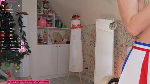 A video of a cozy, festive room with a decorated Christmas tree, a tall, white, striped pole with \"GOAL\" written on it, and floral wallpaper.