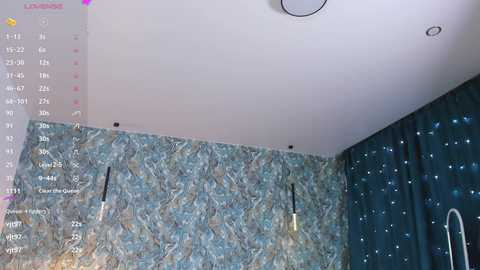 Media: Video of a room with a textured blue-green wall, starry blue curtains, and exposed light bulbs. The ceiling has a circular light fixture.