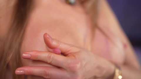 Video of a fair-skinned woman with long brown hair, focusing on her hands gently touching her bare chest, displaying medium-sized breasts. Background is blurred, emphasizing the intimate, delicate moment.