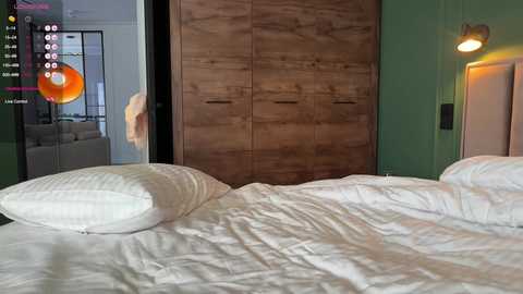 Video of a modern bedroom with a large wooden wardrobe, green walls, a white bed, and a plush pillow. A virtual reality headset is visible in the foreground.