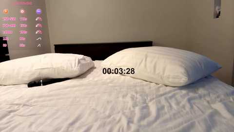 Video of a minimalist, modern bedroom with two white pillows on a neatly made bed. A digital clock displaying \"00:03:28\" is visible on the wall. The background features a beige wall and a dimly lit, partially visible digital display.