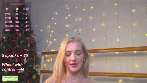 Media: A video of a young woman with long blonde hair, wearing a pink dress, standing in front of a Christmas tree adorned with red and gold ornaments.