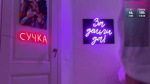 Video of a modern room with a neon sign reading \"30 \u0433\u043e\u0434 \u044e\u043d\u0430\" in Russian. A person in white is partially visible, and a colorful abstract painting hangs on the door.