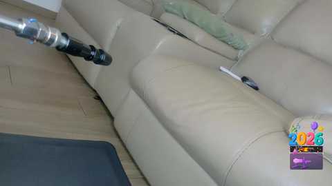 Video of a beige leather sofa with a black extension cord and remote control lying on it, wooden floor, and a colorful \"Happy New Year 2023\" banner in the corner.