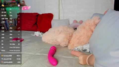 Video of a plush teddy bear lying on a light-colored sofa, surrounded by a pink vibrator and other sex toys, in a dimly lit room with a green light.