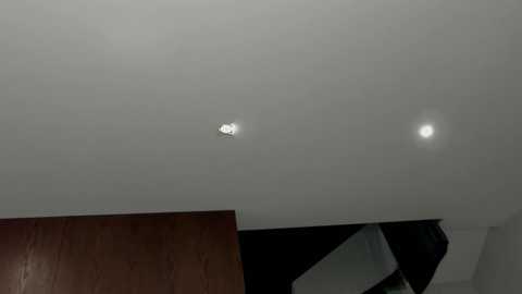 Video of a modern interior ceiling with a bright, circular light fixture in the center, surrounded by a soft, diffused glow. The background shows dark, angular furniture and a wooden panel.