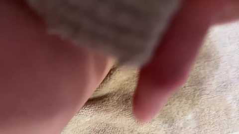Media: A close-up video of a person's hand, with a long fingernail, touching a textured, beige fabric, possibly a blanket or towel. The hand and fabric are the main focus, with a blurred background.