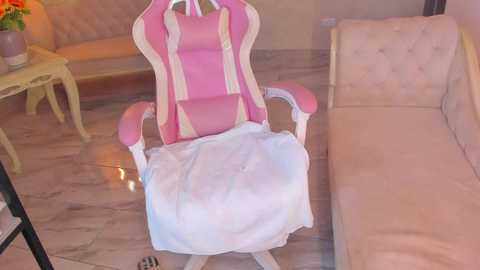 Video of a pink and white gaming chair with a white cloth covering the seat, positioned in a cozy, light-colored living room with beige furniture and a floral-patterned table.
