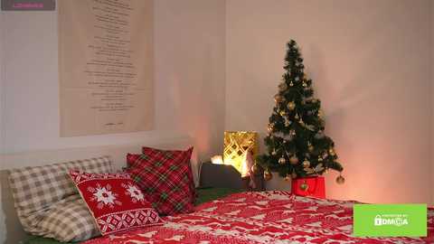 Video of a cozy bedroom with a Christmas tree, red and white patterned bedding, and a lit candle on a nightstand, creating a warm, festive atmosphere.