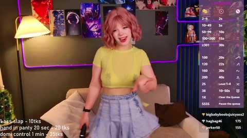 Video of a smiling woman with pink hair in a yellow crop top and high-waisted skirt, sitting on a couch in a dimly lit room with neon lights.