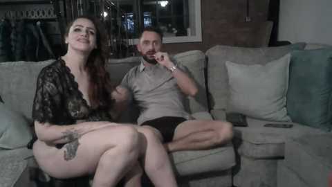 Media: Video of a smiling, tattooed white woman in a black lace top and a white man with a beard in a grey shirt, sitting on a beige sofa.