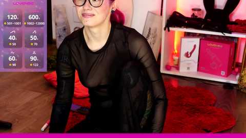 Video of a fair-skinned woman with glasses, wearing a sheer black mesh top, kneeling on a red shag rug in a dimly lit room with erotic items on shelves.