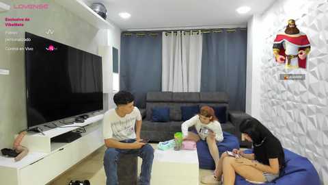 Video of a modern living room with three young adults, two on a couch, one on a bean bag, watching TV.