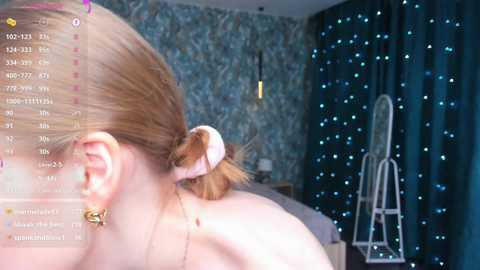 Media: Video of a blonde woman with a ponytail, seen from behind, in a room with teal curtains and a ladder, streaming on a screen.