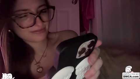 Video of a woman with long dark hair, glasses, and a black panda-themed phone case, smiling.