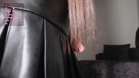 Media: A close-up video of a person's long, straight, brown hair, styled into a sleek ponytail, partially obscured by a black leather jacket. Background shows a dark couch and a partially visible, plain wall.
