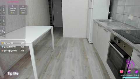 Video of a modern kitchen with white cabinets, gray tiles, and wooden floor. A white table and a stainless steel oven are visible. The image appears to be a virtual reality screenshot.