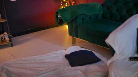 A cozy, dimly-lit room with a plush green velvet sofa, a white fluffy rug, a dark pillow, and a warm, ambient yellow light in the background.