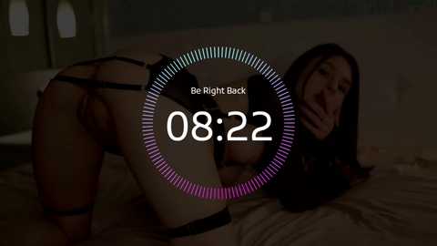 A dimly lit video shows a woman in black lingerie, bent over a bed, with \"Be Right Back\" text overlay, set in a dark, dimly lit room.