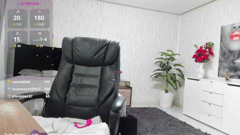 Video of a modern bedroom with a black leather recliner, white textured wallpaper, a white dresser, a potted plant, and a framed artwork on the wall.
