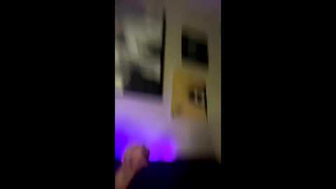 A blurry, nighttime video of a person's hand holding a lighted cigarette, with a purple light illuminating the scene. The background is dark and indistinct, creating a mysterious, slightly grainy atmosphere.