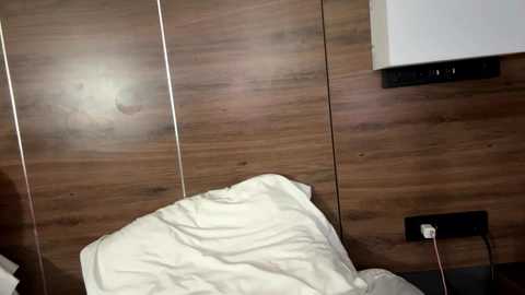 Video of a bedroom wall with a wooden texture, featuring a white pillow and a power outlet on the right.