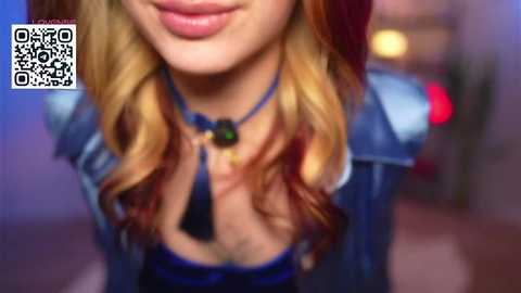 Video of a woman with wavy blonde hair, wearing a blue crop top and denim jacket, smiling. Background is blurred with a QR code watermark.