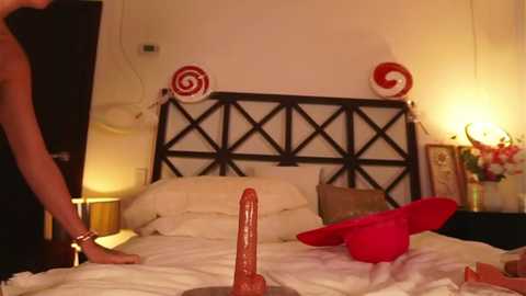 Video of a cozy, dimly-lit bedroom with a woman in a black dress, a large red dildo on the bed, and festive candy-themed decorations.