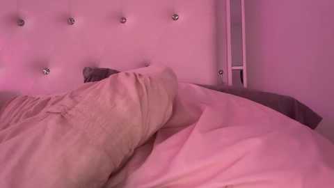 A video of a plush, tufted headboard with pink lighting, featuring a beige blanket and a gray pillow, creating a soft, cozy atmosphere.