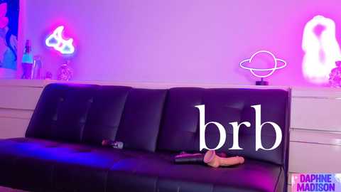 Video of a modern room with a black leather couch and neon signs; \"brb\" text on the couch, purple and pink lights, and a \"PHAT PHUCK MASTERS\" watermark.