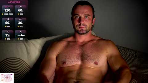 Video of a shirtless, muscular white man with short dark hair, sitting on a bed with a striped pillow. Background includes a digital overlay with fitness stats and a \"Love Island\" logo.