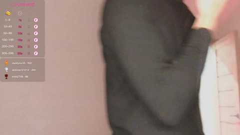 A video of a person's arm and hand, wearing a dark jacket, against a light wall with a digital display showing date and time in the background.