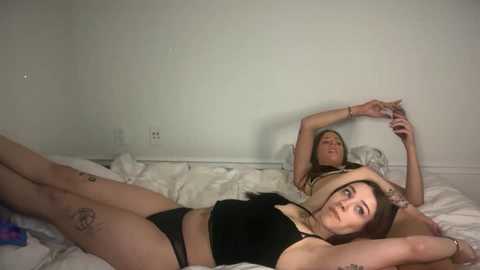 Video of two women in black lingerie, one lying on a bed, the other standing, forming a heart shape with their arms.