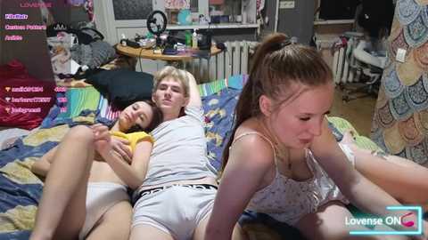 Media: Video of a young couple on a bed, a man wearing white shorts and a woman in a white tank top, surrounded by a messy room with gaming equipment and plushies in the background.