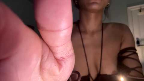 Video of a close-up of a hand with a large, prominent finger and a woman's bare, partially exposed cleavage in the background, wearing a black off-shoulder top.