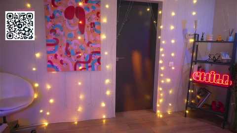 Video of a cozy, softly lit room with yellow string lights, a vibrant abstract wall art, a black door, a white chair, a black metal shelf with books, and a glowing \"Sushi\" sign.