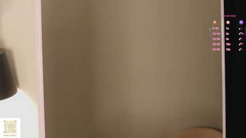 Video of a beige wall with a small, white QR code and a pink, vertical, digital text overlay in the upper right corner.