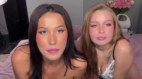 Video of two young women with light skin, one with long black hair and the other with long blonde hair, making pouty faces.