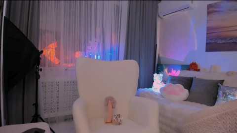 Video of a dimly lit, modern living room with a white armchair featuring a dildo in its armrest, grey couch, and decorative pillows. Soft, ambient lighting creates a cozy, intimate atmosphere.