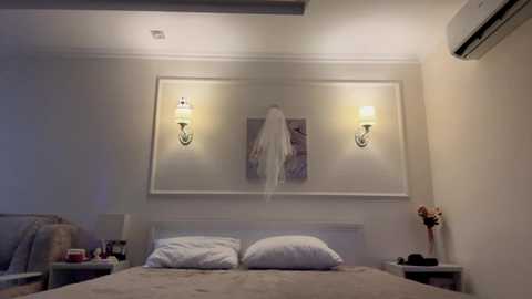 Video of a modern, minimalist bedroom with a white bed, two wall-mounted lamps, a white robe hanging, and an air conditioning unit on the right wall.