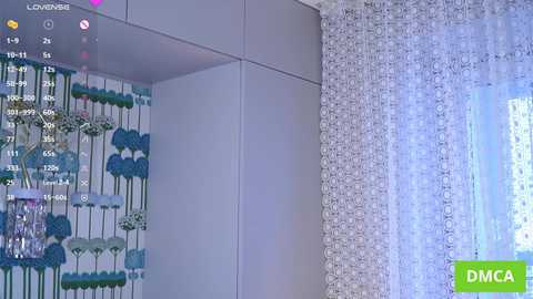 A video of a room corner featuring a white wall with a floral mural and a sheer curtain, showing a live feed of a virtual space with a blue theme.