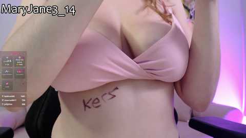 A video of a fair-skinned woman with a pink bra revealing a tattoo of \"Ker\" on her stomach, taken indoors with purple lighting.